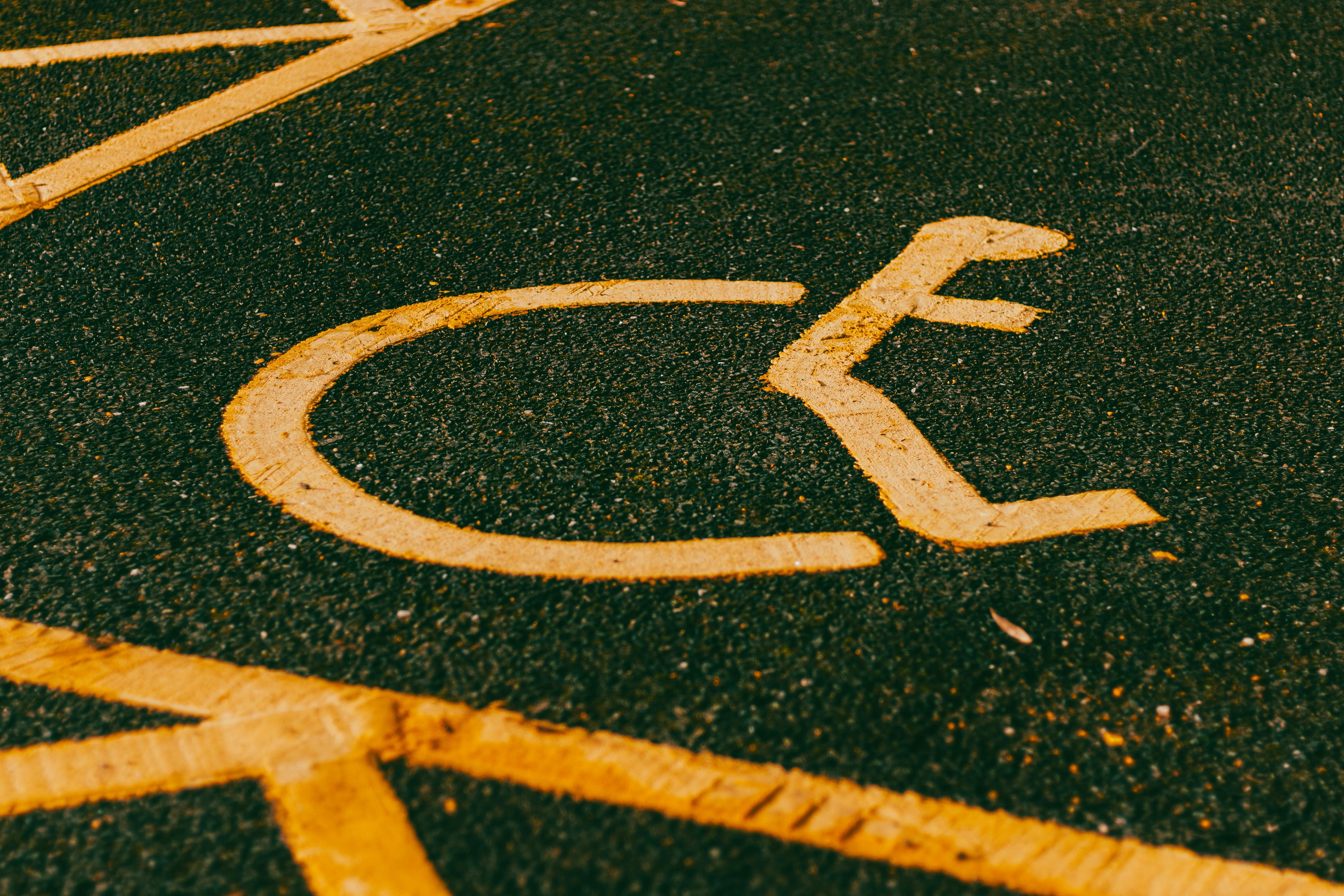 The International Symbol of Access painted in yellow on asphalt pavement.